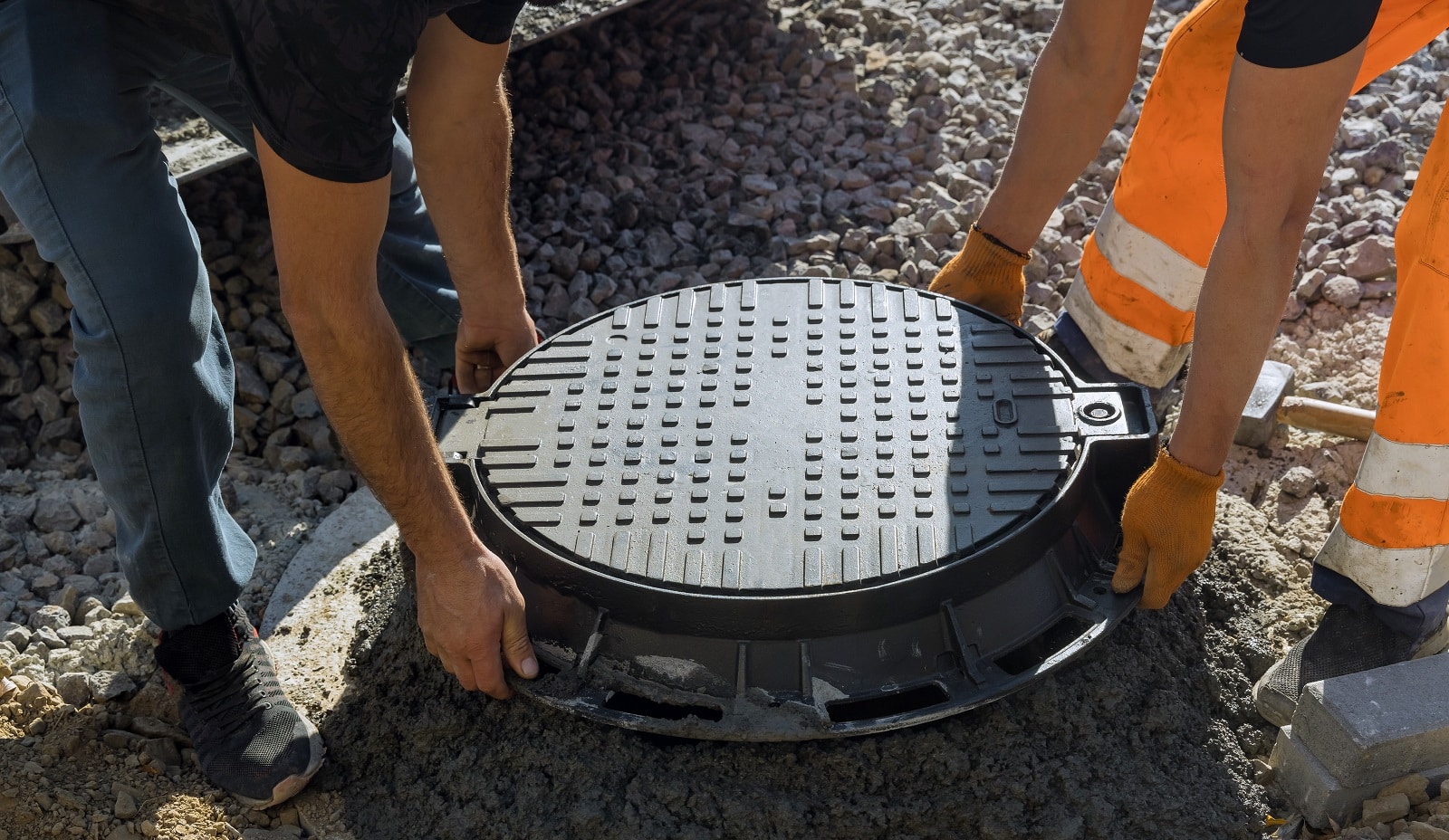 a worker installs a sewer manhole on a septic tank made of concrete rings